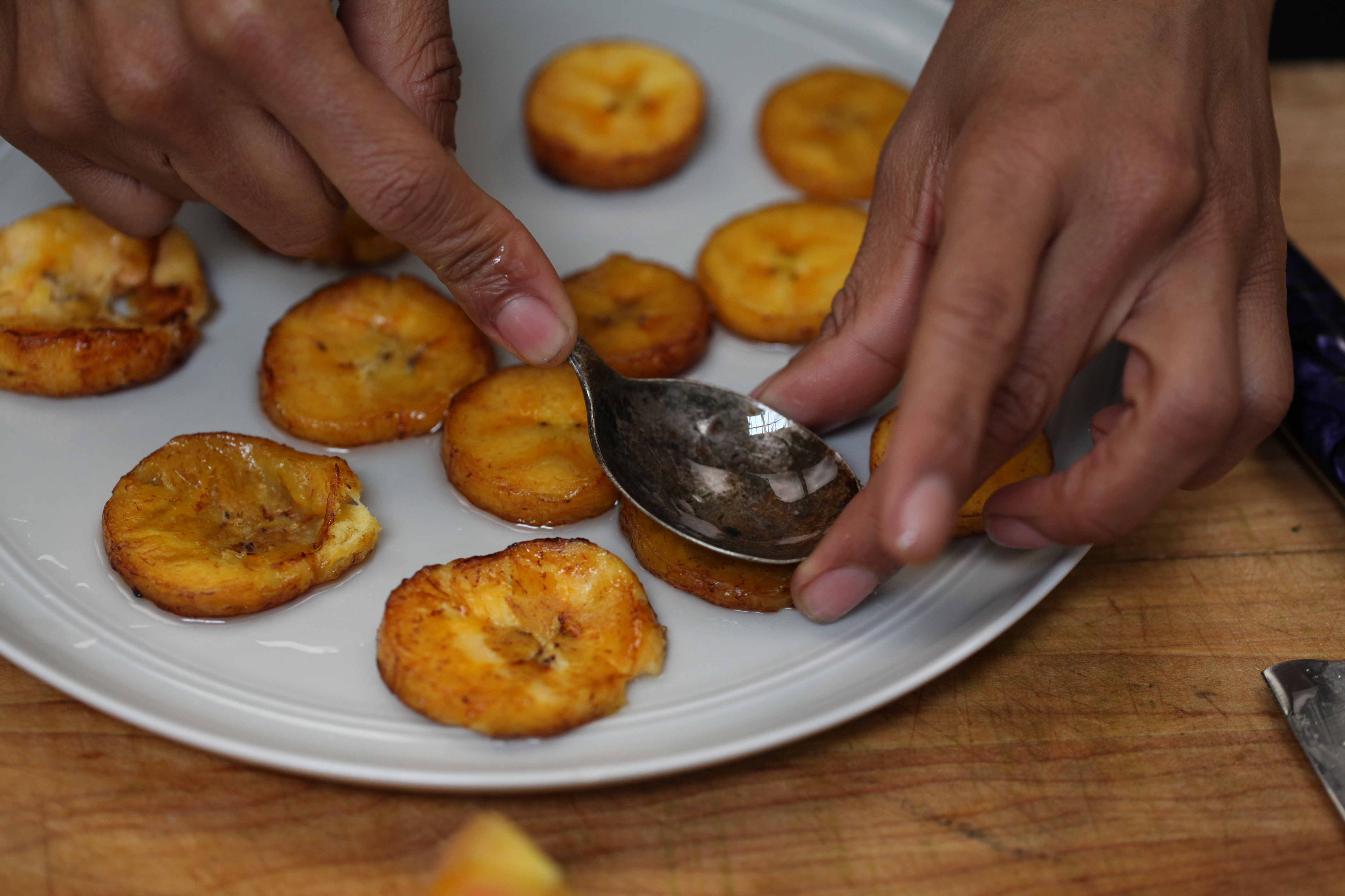 chef ashleigh shanti smashing once-fried plantains with a spoon