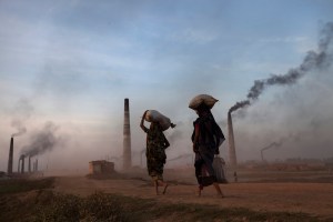 Zwei junge Bangladescherinnen vor rauchenden Fabrikschloten