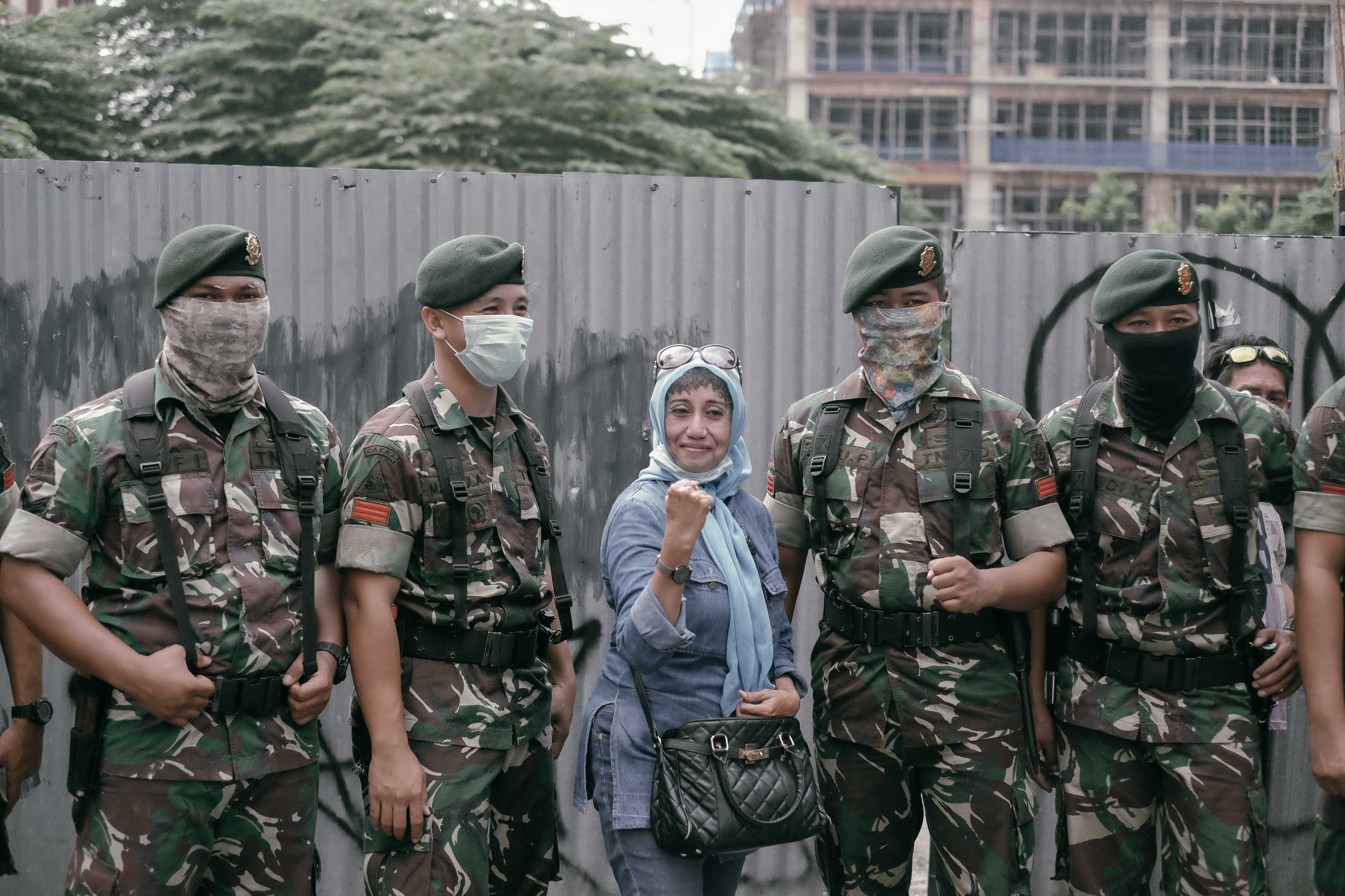 A woman poses with the military at the Jakarta election riots.