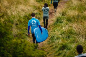 People carrying surfboards through grass