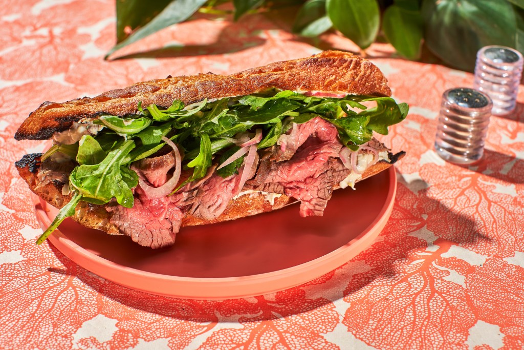 a plate holding a baguette sandwich with flank steak, arugula, and homemade horseradish cream sauce