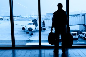 A stock photo of a traveler looking out the airport window at a plane.