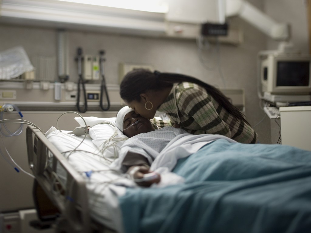 black woman kissing her son in a hospital bed