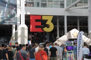 A photo from within the LA Convention Center, "E3" hanging from the ceiling as a crowd of people walk below it.