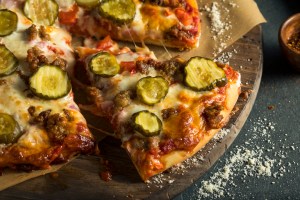 a Hamburger Pizza with Beef, Pickles, and Onions on a dark brown wooden cutting board