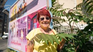 Eine ältere Frau mit roten Haaren steht vor einer bunten Wand