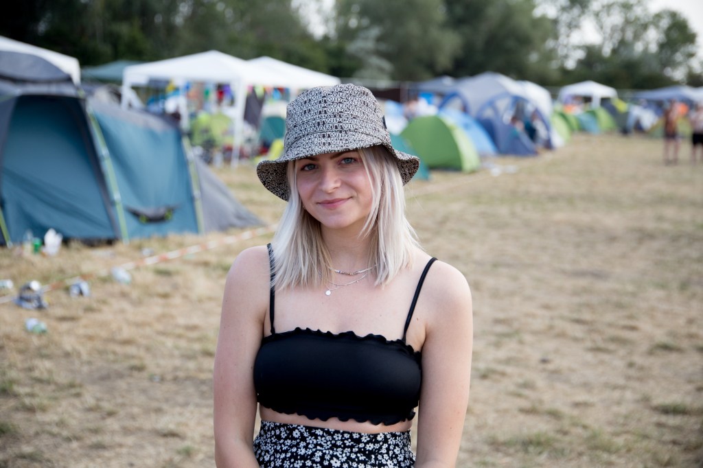 Eine Frau mit Hut steht vor einem Zeltplatz