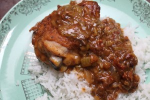 a bowl of smothered chicken thighs on white rice, made by chef kia damon