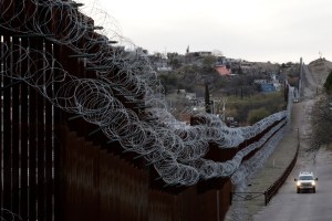 A Customs and Border Control agent patrols on the US side of a razor-wire-covered border wall that separates Nogales, Mexico from Nogales, Ariz.