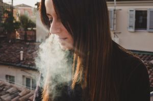 perempuan sedang menghembuskan uap vape dari hidung