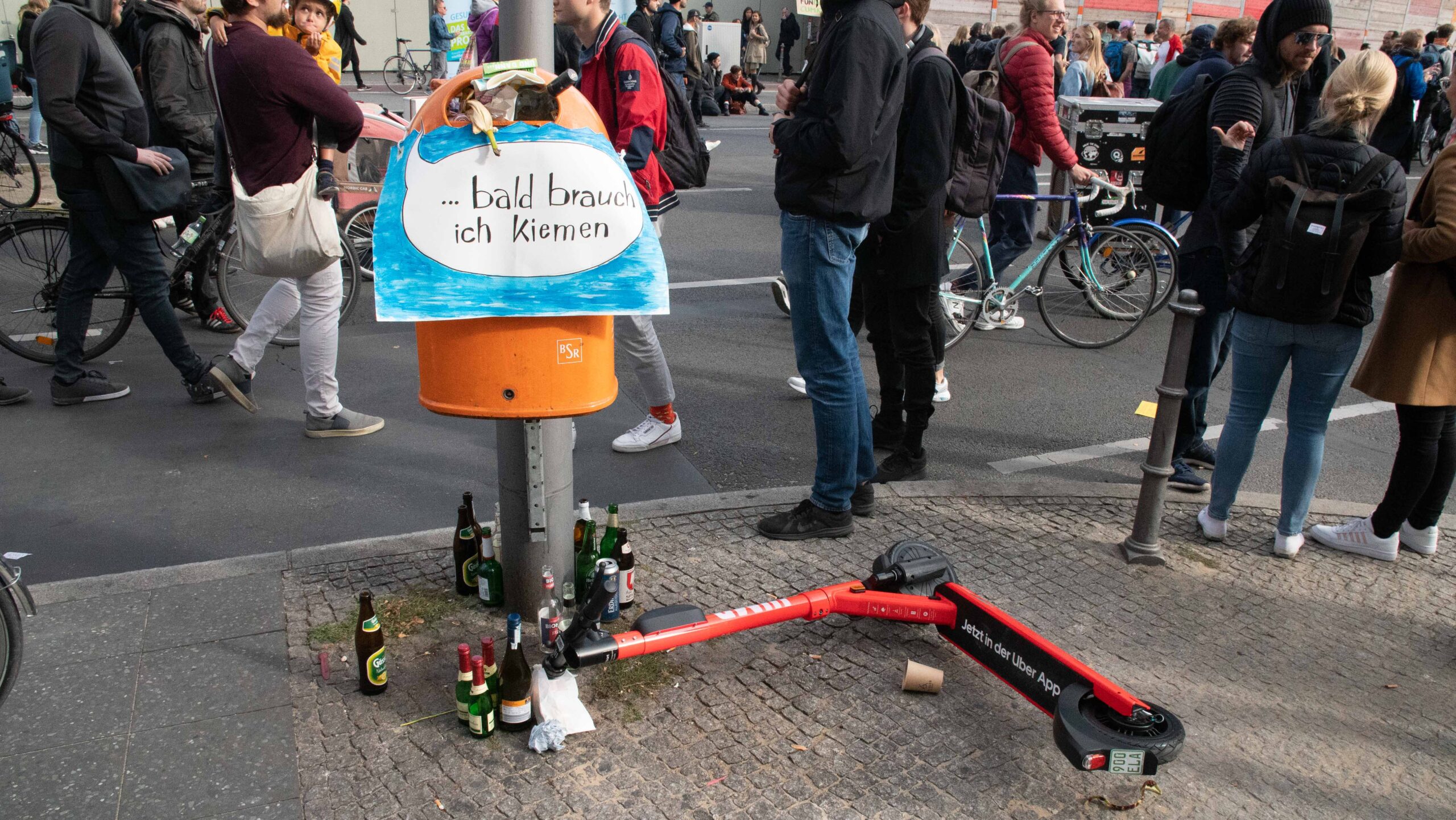 Ein voller Müllereimer und ein E-Scooter beim Klimastreik