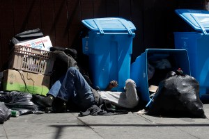 In this Aug. 21, 2019, file photo, a homeless man sleeps in front of recycling bins and garbage on a street corner in San Francisco.(AP Photo/Jeff Chiu, File)​