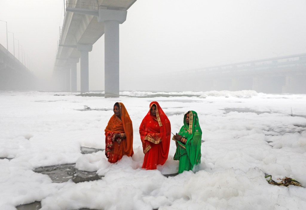 Tiga perempuan bersembahyang di Sungai Yamuna yang tercemar