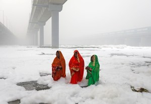 Tiga perempuan bersembahyang di Sungai Yamuna yang tercemar