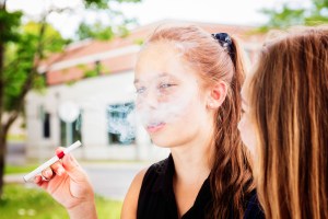 A teenage girl smokes an e-cigarette