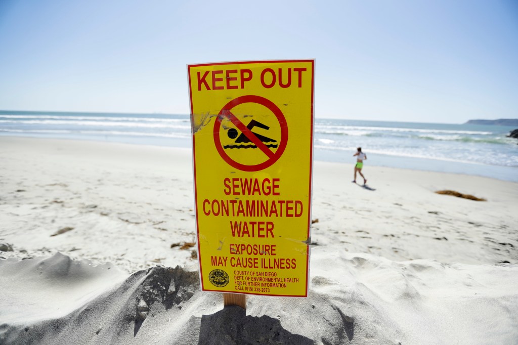 A sign warns of sewage contaminated ocean waters on a beach. (AP Photo/Gregory Bull)​