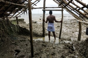 Een man staat in een vervallen huis en kijkt uit over het water.