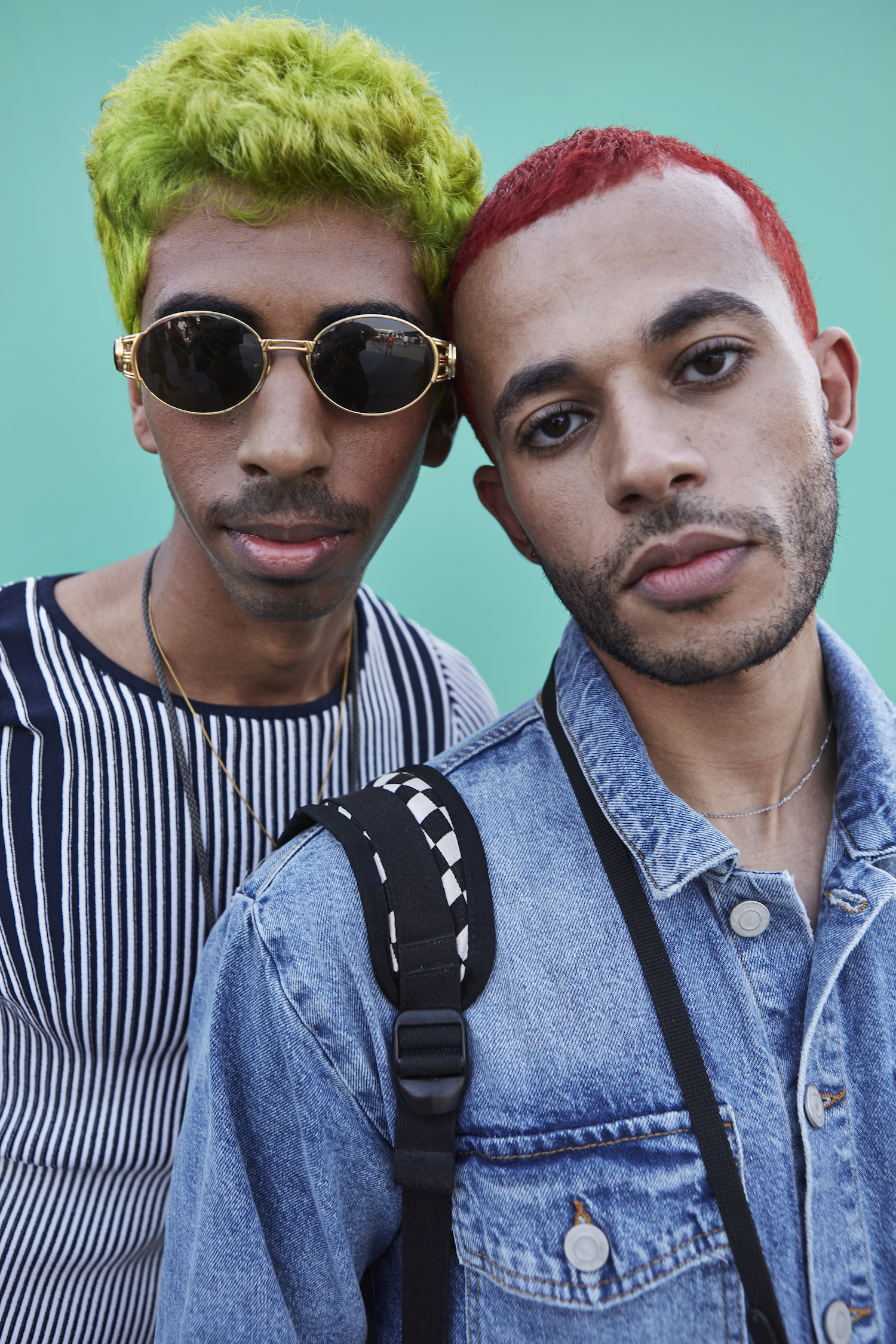 Two young men stare directly into the camera. The man on the left has green hair and wears sunglasses, the man on the left has short red hair.