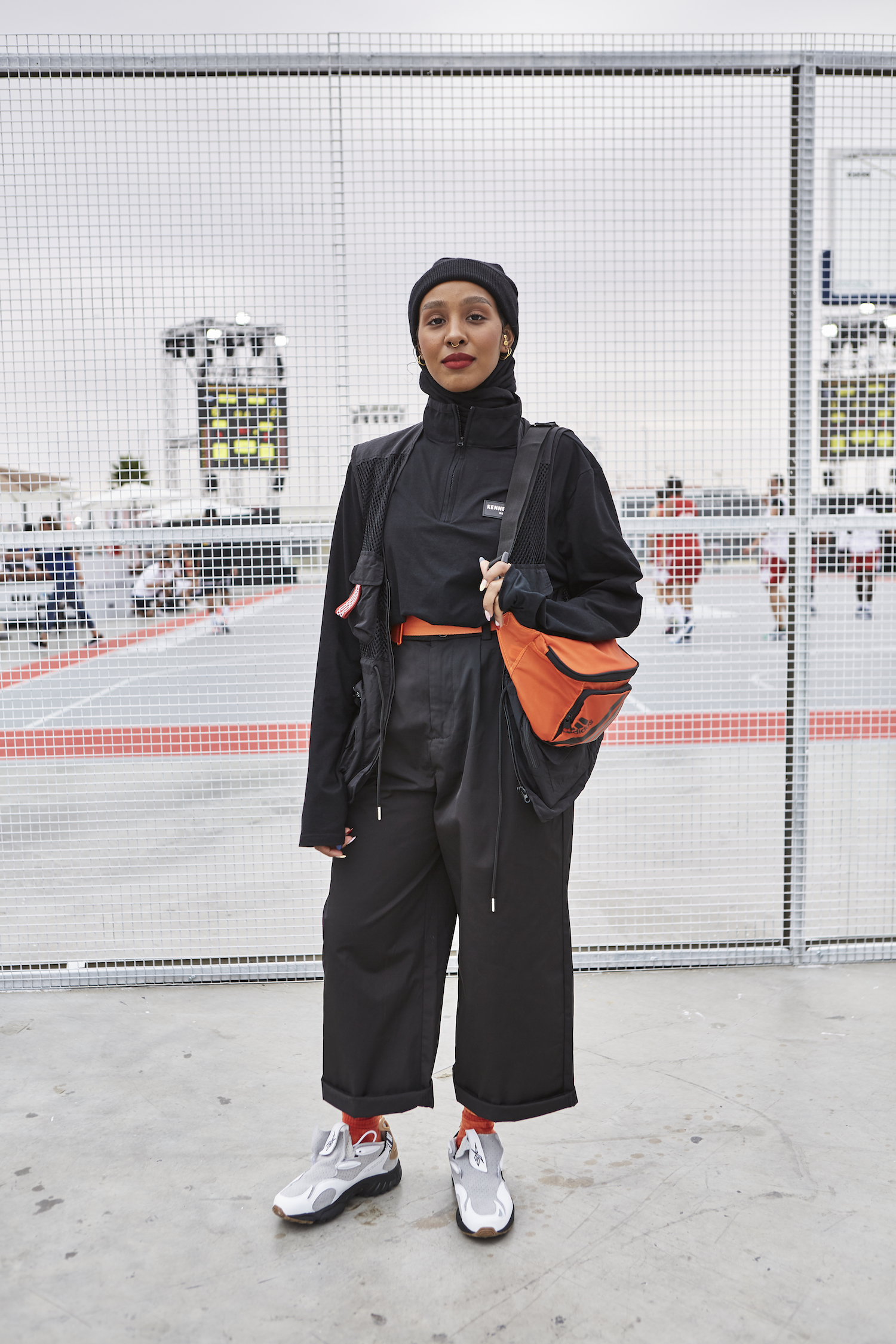 A woman wearing a hijab in black and orange streetwear look.