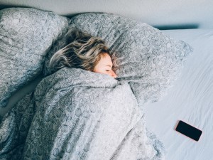 Woman sleeping under covers with her phone next to her in bed.