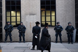 In this Dec. 11, 2019 file photo, Orthodox Jewish men pass New York City police guarding a Brooklyn synagogue prior to a funeral for Mosche Deutsch in New York.