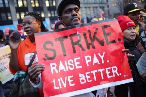 A man holding a sign that reads STRIKE. RAISE PAY. LIVE BETTER.