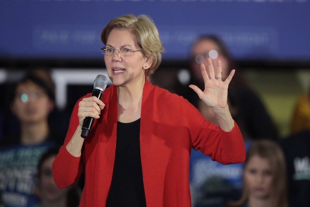 Senator Elizabeth Warren holding a microphone and raising her hand.