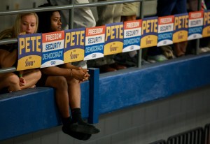 Two young women sit dejectedly amongst banner for candidate Mayor Pete