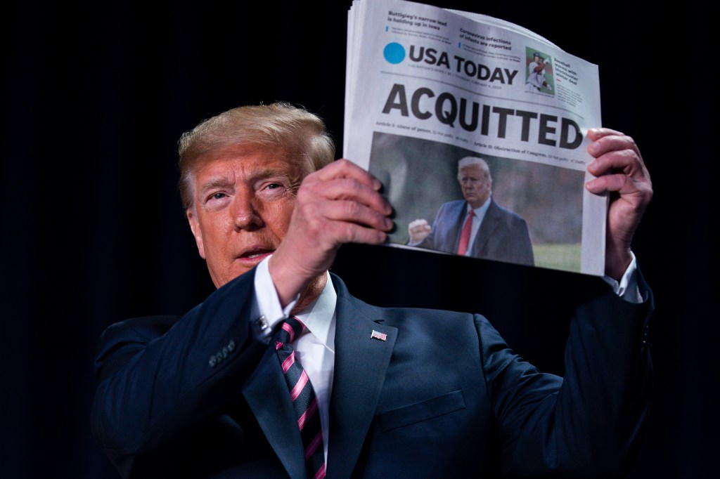 President Donald Trump holds up a newspaper with the headline that reads "ACQUITTED" at the 68th annual National Prayer Breakfast, at the Washington Hilton, Thursday, Feb. 6, 2020, in Washington. (AP Photo/ Evan Vucci)​