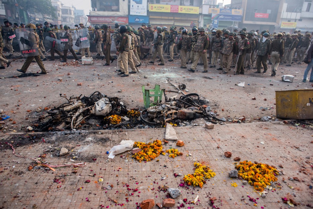 Indian police and paramilitary forces walk past charred bikes and flowers scattered on a road which was destroyed in clashes between groups supporting and opposing the Citizenship Amendment Act on February 24, 2020 in Delhi, India.