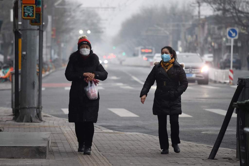 Women wear face masks to protect against the COVID-19 coronavirus as they walk on a sidewalk on a polluted day in Beijing on February 20, 2020.