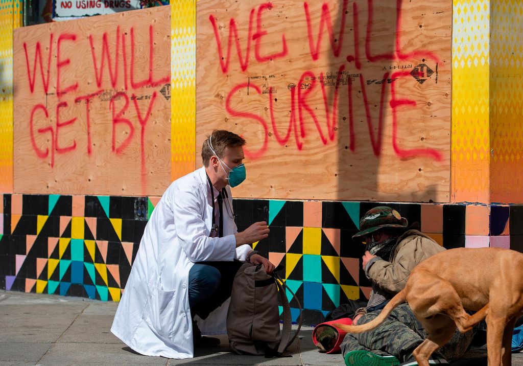 A doctor in a facemask talks to a man on the street.