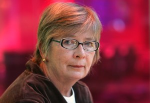 A portrait of Barbara Ehrenreich against a blurred red background.