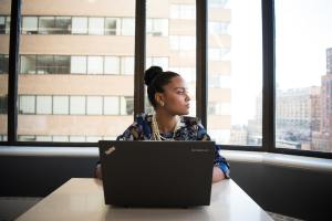 Perempuan menengok ke arah samping dengan laptop di hadapannya