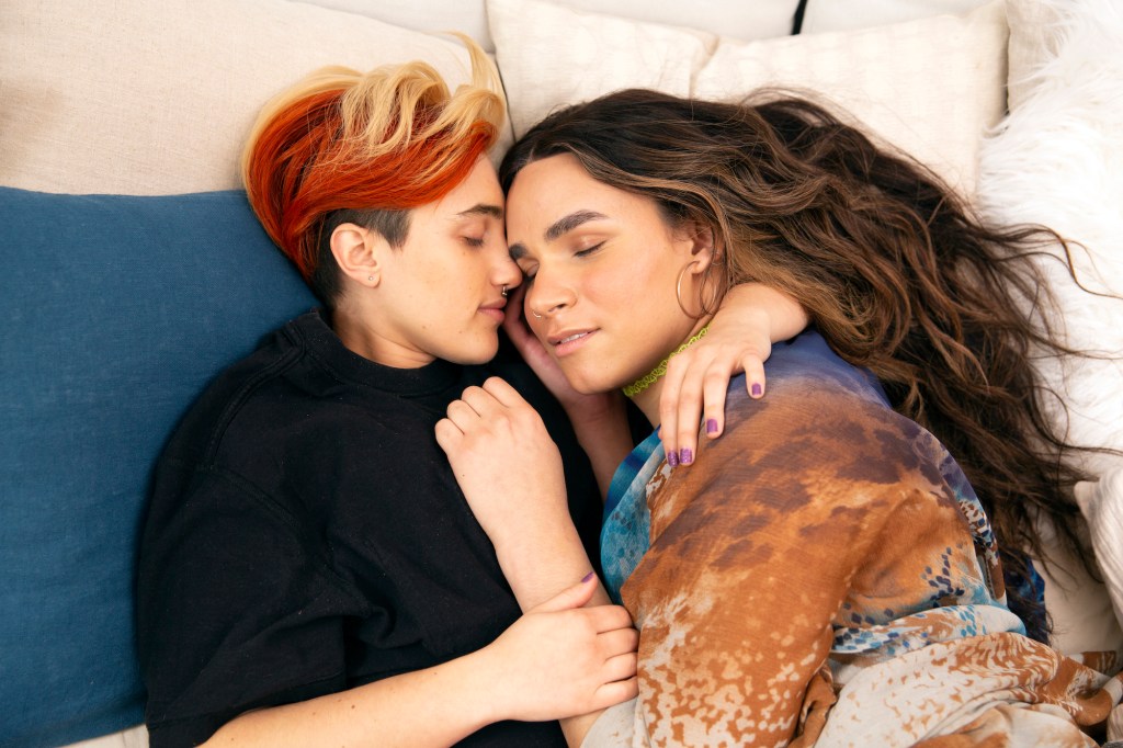 A transmasculine gender-nonconforming person and transfeminine non-binary person sleeping together in bed