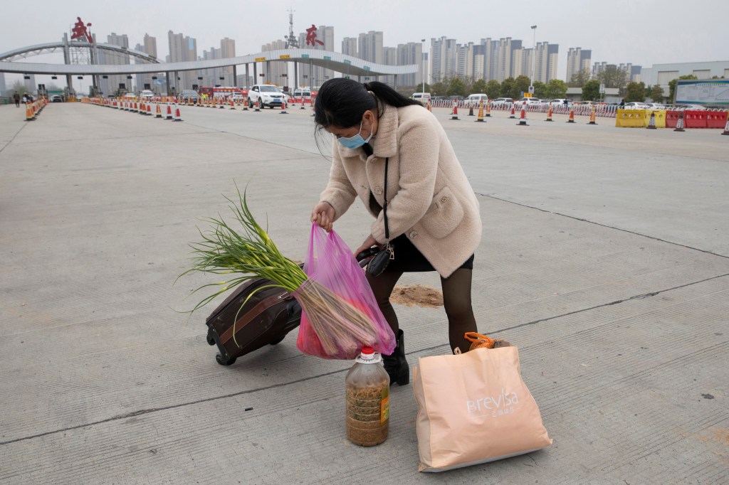 Una mujer que lleva una maleta y verduras ingresa a la ciudad de Wuhan, China