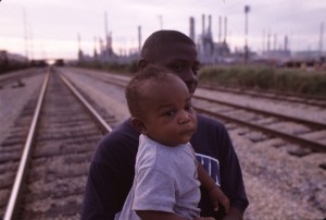 African American man and boy in Cancer Alley, with  oil and chemical refinery plants in the background