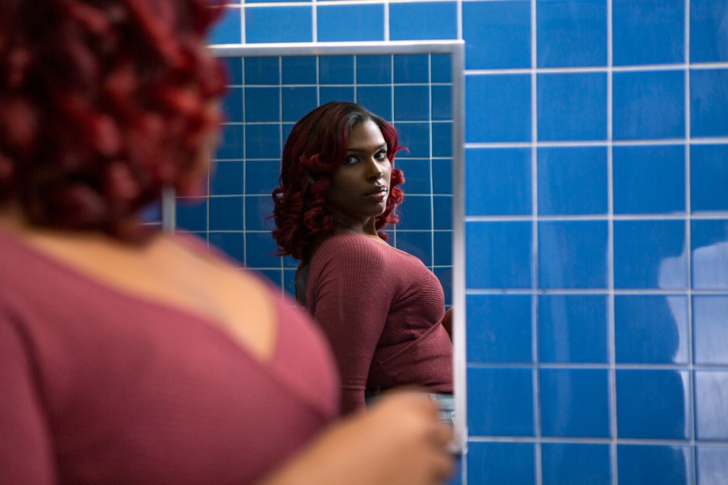 A young transgender woman looking at her reflection in a bathroom mirror