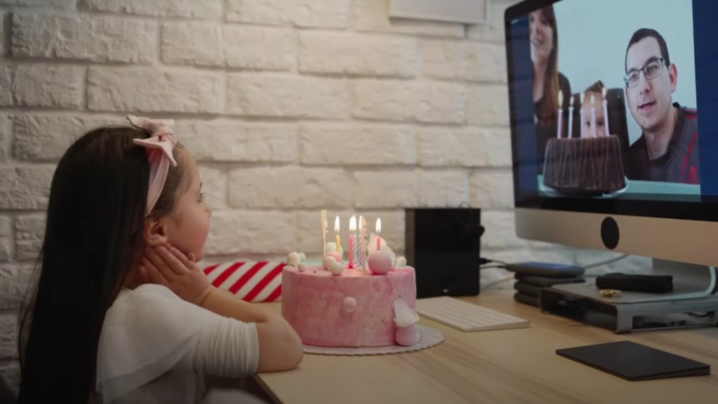 Anak perempuan menghadap ke kue ulang tahun sambil video call