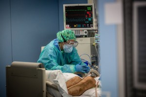 A medical worker wearing protective face mask, goggles and scrubs, tends to a patient on a ventilator diagnosed with Covid-19