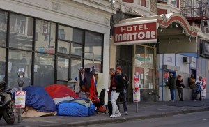 Pedestrians walk to the edge of the sidewalk to avoid stepping on people in tents and sleeping bags on Monday, April 13, 2020, in the tenderloin area of San Francisco. Local governments have begun moving large numbers of homeless into hotels as part of Op