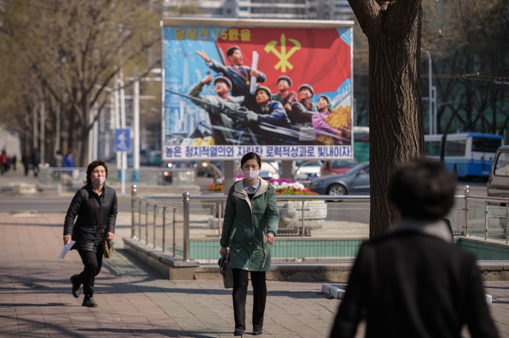 Dua orang maskeran berjalan di depan poster propaganda yang terpasang di jalanan Pyongyang pada 9 April 2020. Kim Won Jin / AFP