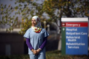 A doctor in scrubs and hijab stands outside an emergency room