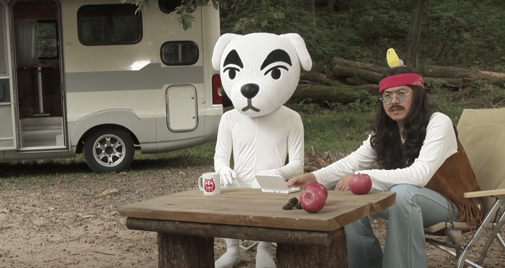 Two human beings cosplaying as KK Slider and Harv from Animal Crossing posing at a picnic table.