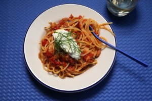 a white bowl of spicy sardine spaghetti topped with ricotta and dill