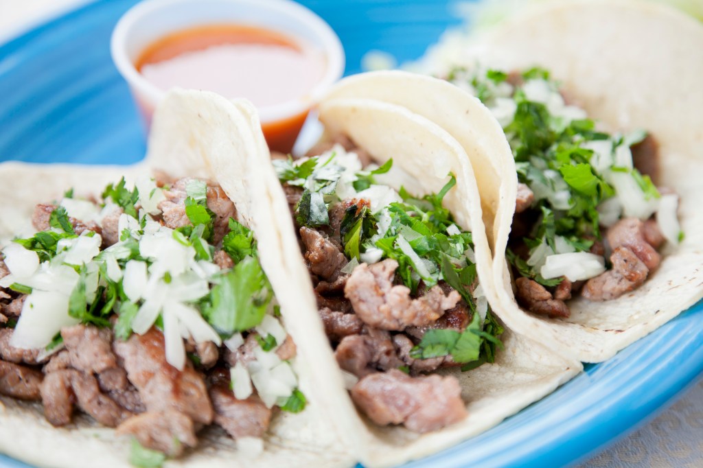 a plate of three steak tacos topped with raw onions and cilantro