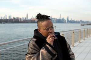 A transmasculine person standing by the water and smoking a Juul close up