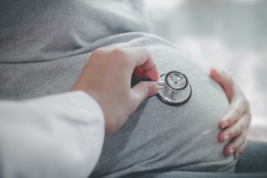 Cropped Hand Of Doctor Examining Pregnant Woman Belly With Stethoscope - stock photo