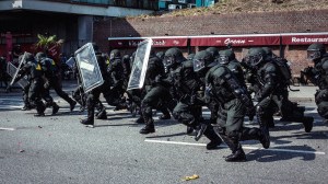 Schwarz vermummte Polizisten laufen mit hochgehaltenen Schutzschilden während der G-20-Proteste in Hamburg über eine Straße.