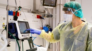 A medical worker covered in PPE gear reads a screen in a hospital room.